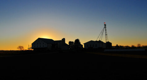 The sun drops behind a barn and silo putting them in shadows in Carlisle, PA