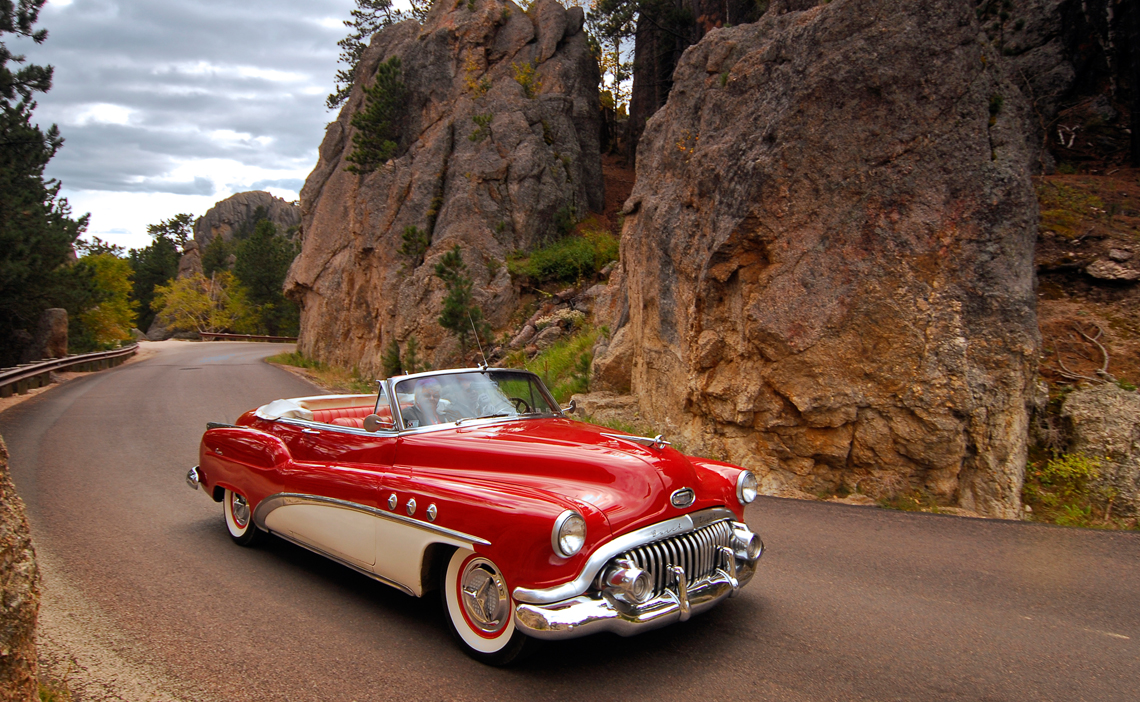 A classic car cruises past a rocky side of the Black Hills near Rapid City.
