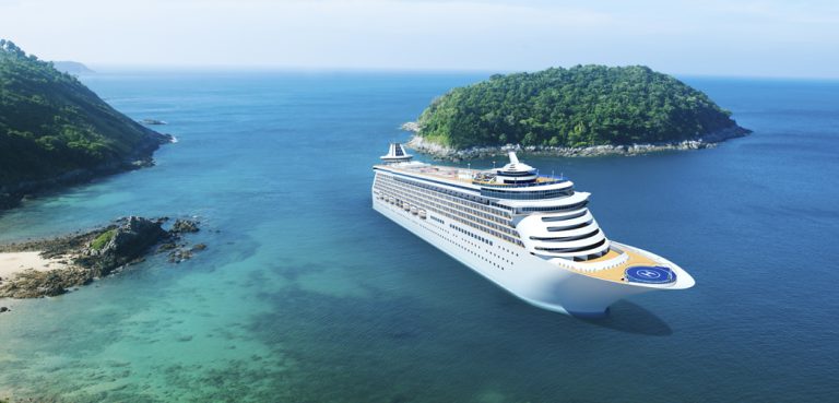 A cruise ship floats in blue water between a beach and an island.