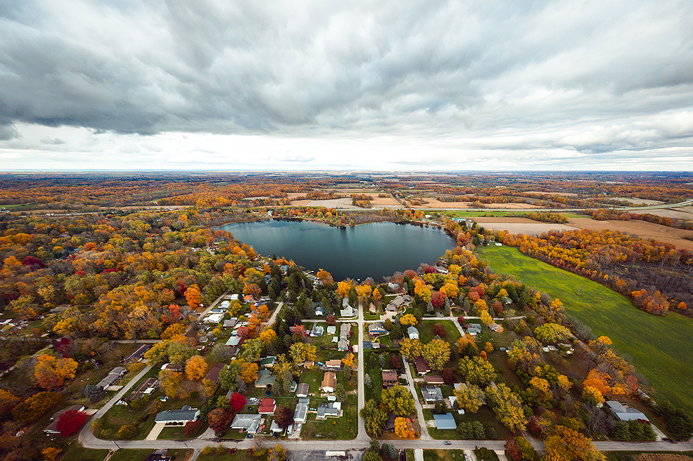 Beautiful full panoramic aerial view of the heart shaped Saugany Lake in Indiana surrounded by residential homes and autumn colored trees or foliage with fluffy white clouds in the sky above