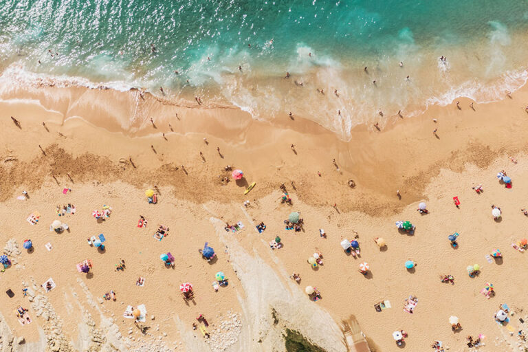 Stock photo of beach lined with umbrellas and people during summer