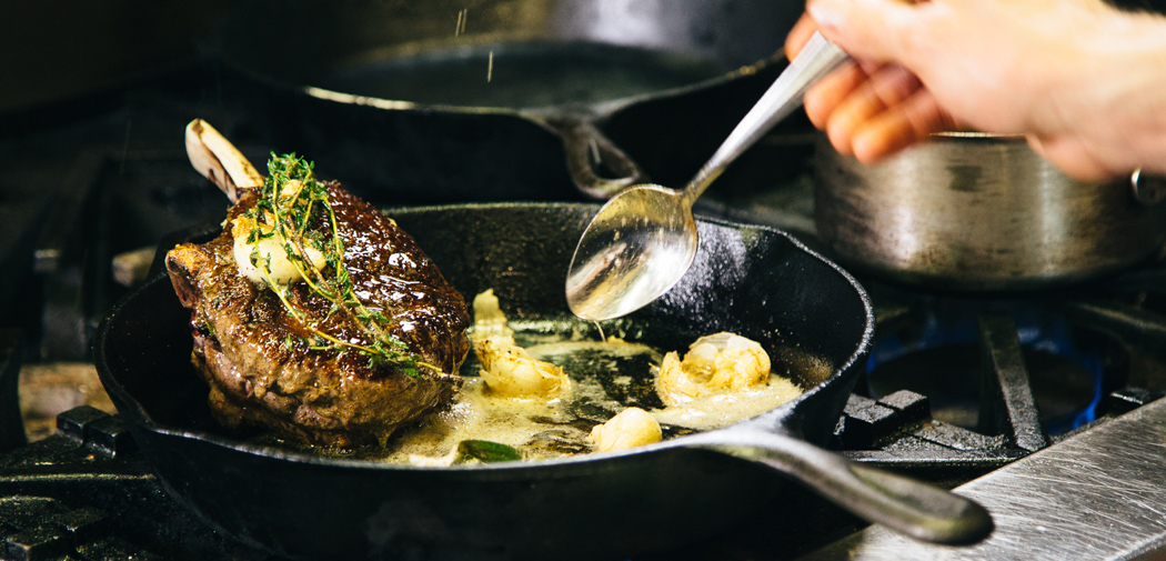 Lamb chop sizzles in a cast iron pan at The Grey Plume in Omaha, NE.