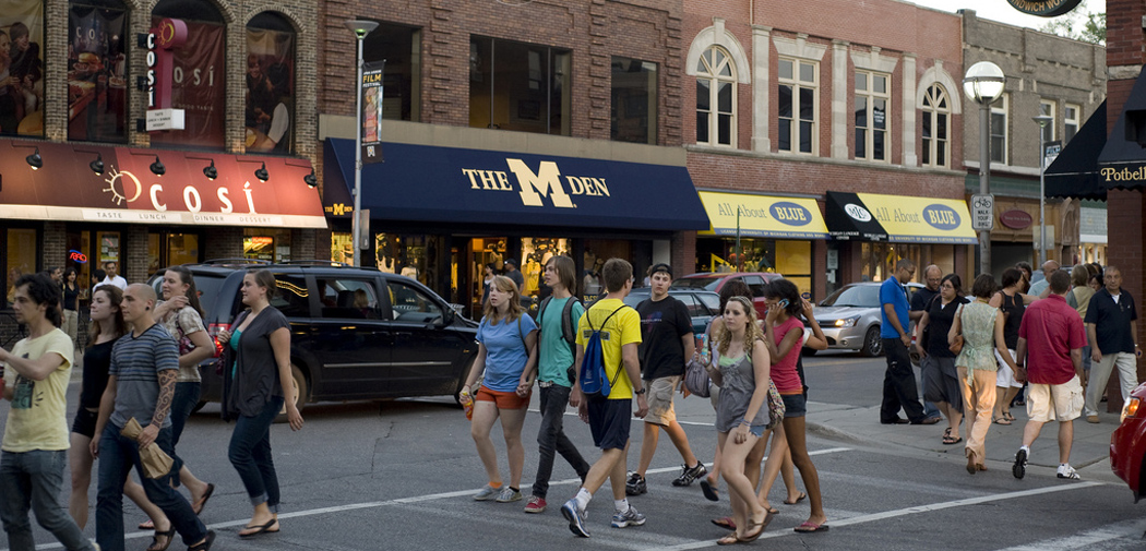 People cross the street in downtown Ann Arbor in front of a store called The M Den