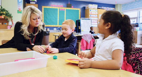 Teacher helps two young students at a table in Worcester MA