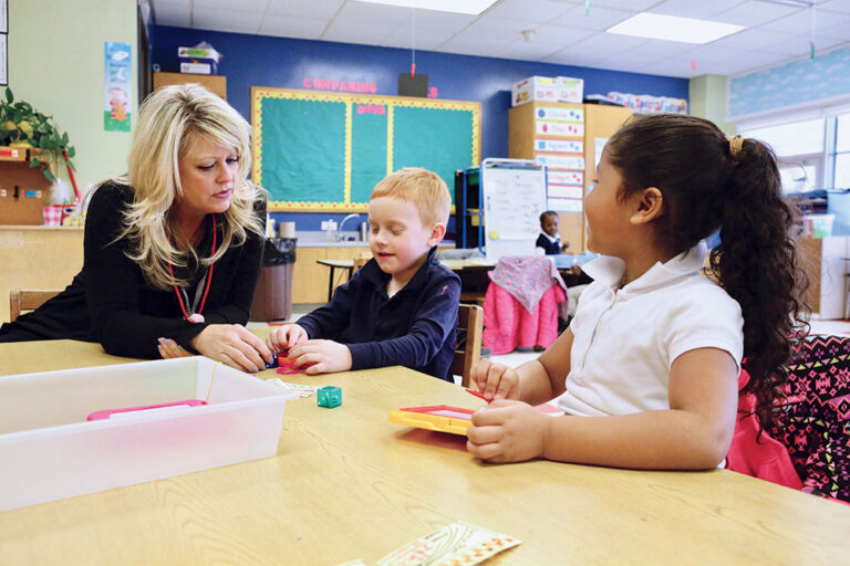 Teacher helps two young students at a table in Worcester MA