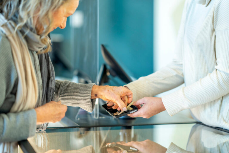 A female retail clerk in a legal cannabis shop, holds out product for a customer to view. The mature female customer is dressed casually and reaching for a joint to look at it closer.