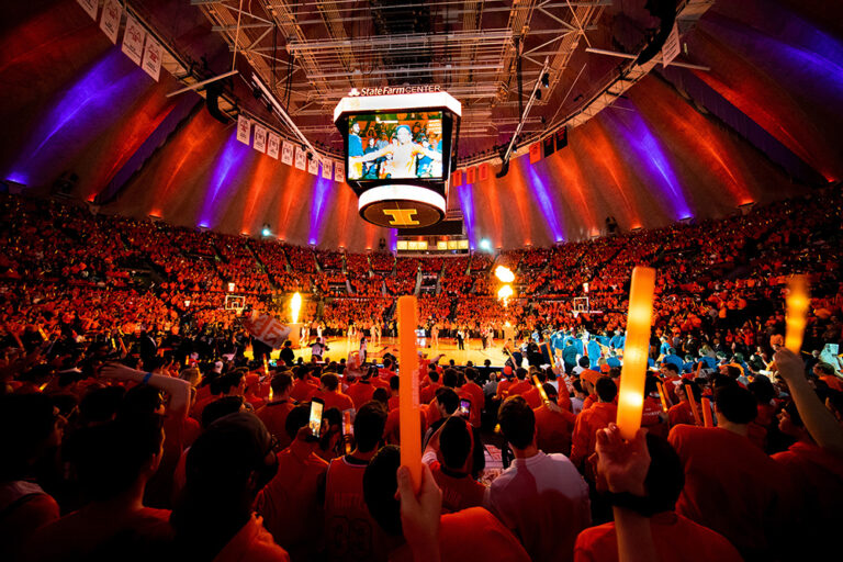 Glow sticks and plenty of Illini pride light up State Farm Center as members of the Orange Krush cheer on the University of Illinois men's basketball team. The work of the Orange Krush does more than just help the team on the court. As a branch of the registered student organization, Illini Pride, at the University of Illinois at UrbanañChampaign, Orange Krush members fund raise, donating more than $2 million to help local and national charities.
