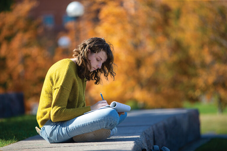 Student writes in a notebook on the University of Cincinnati campus in the Northern Kentucky region.