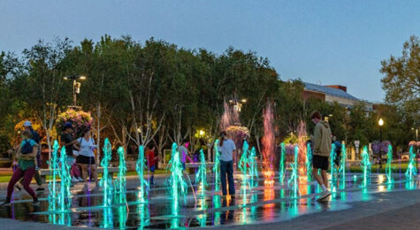 Families play in City Park Fountain in downtown Beaverton, OR, at dusk.