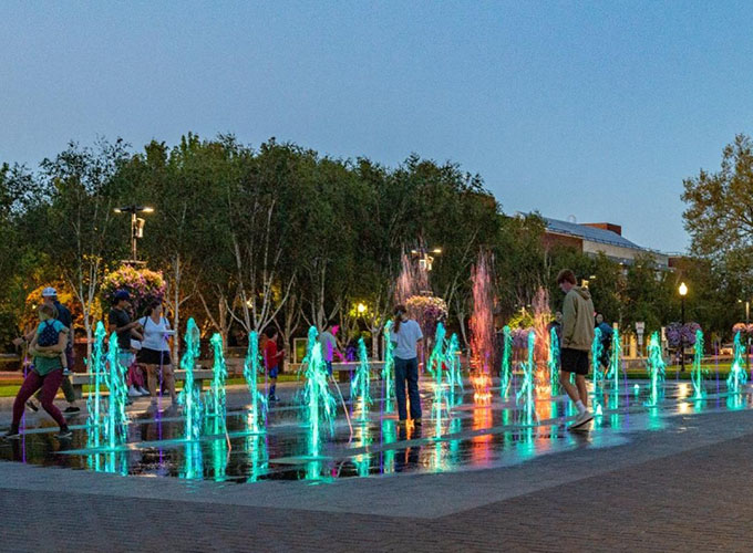 Families play in City Park Fountain in downtown Beaverton, OR, at dusk.