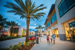 Families stroll along the sidewalks past the storefronts at One Daytona in Daytona Beach, Florida.